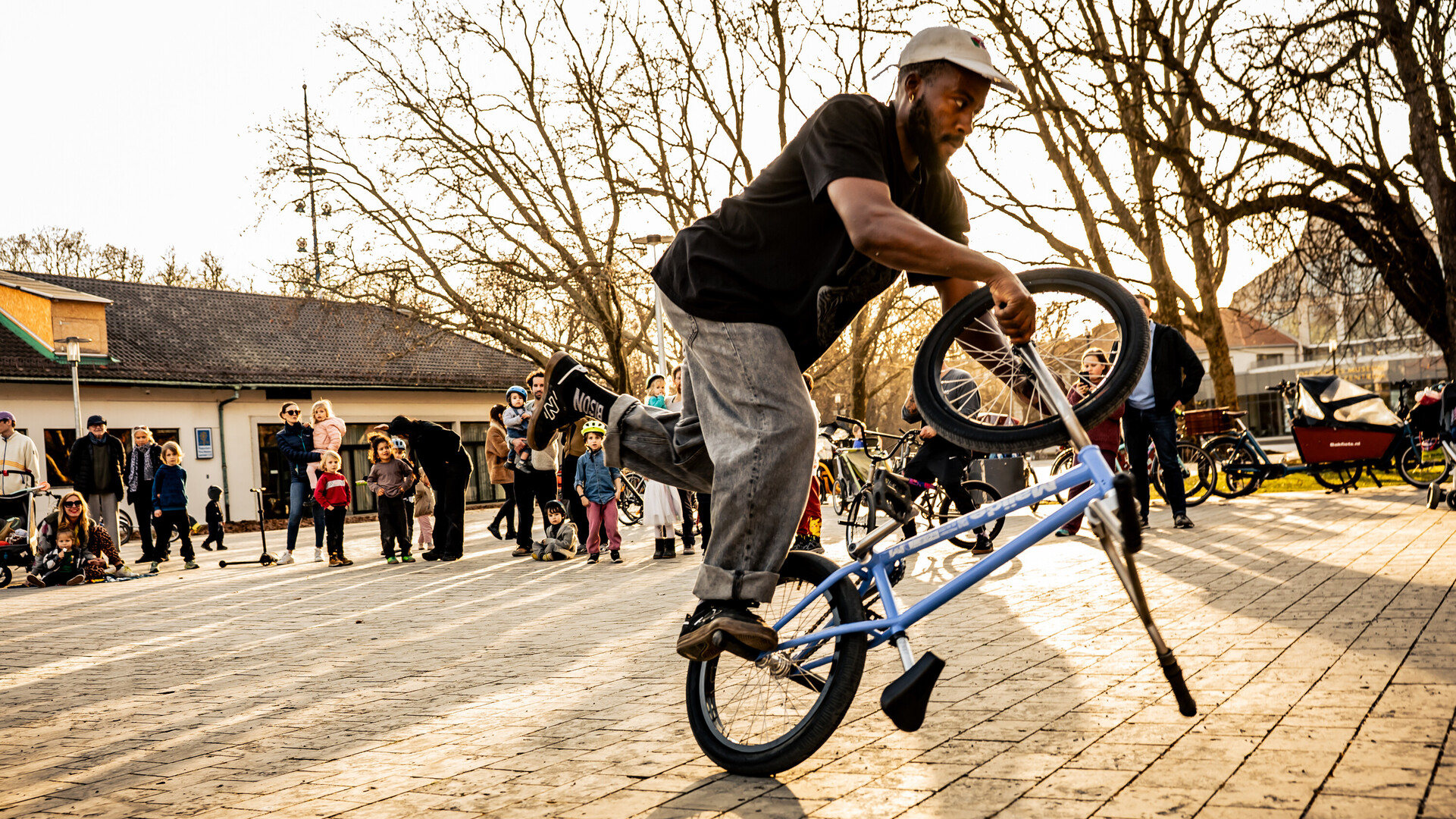 Omari Cato performing a flatland BMX trick on a city square with people watching.