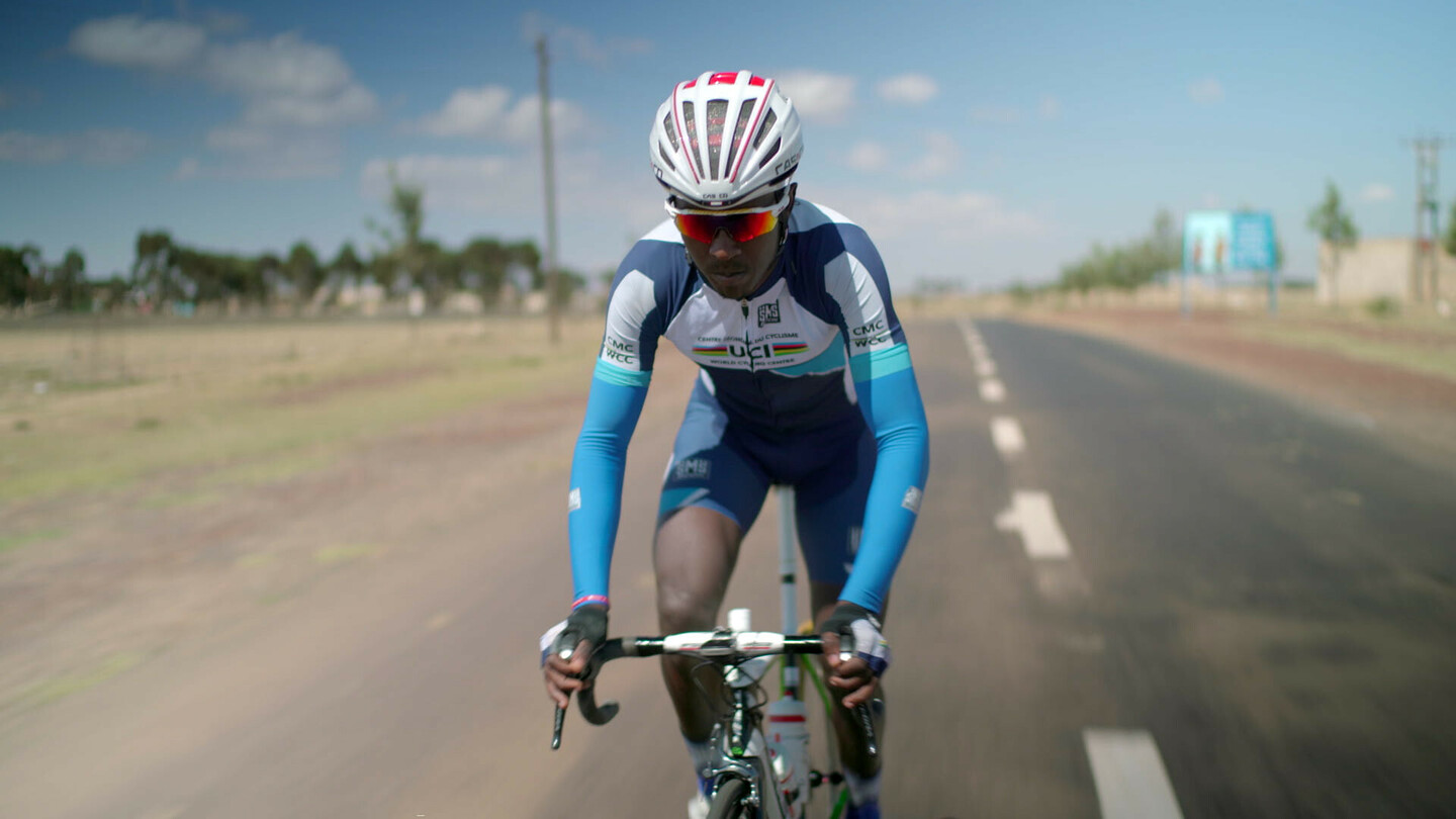 Biniam Girmay faisant du vélo de route sur une route ouverte, vêtu d'une tenue de cyclisme UCI bleue et blanche avec un casque.